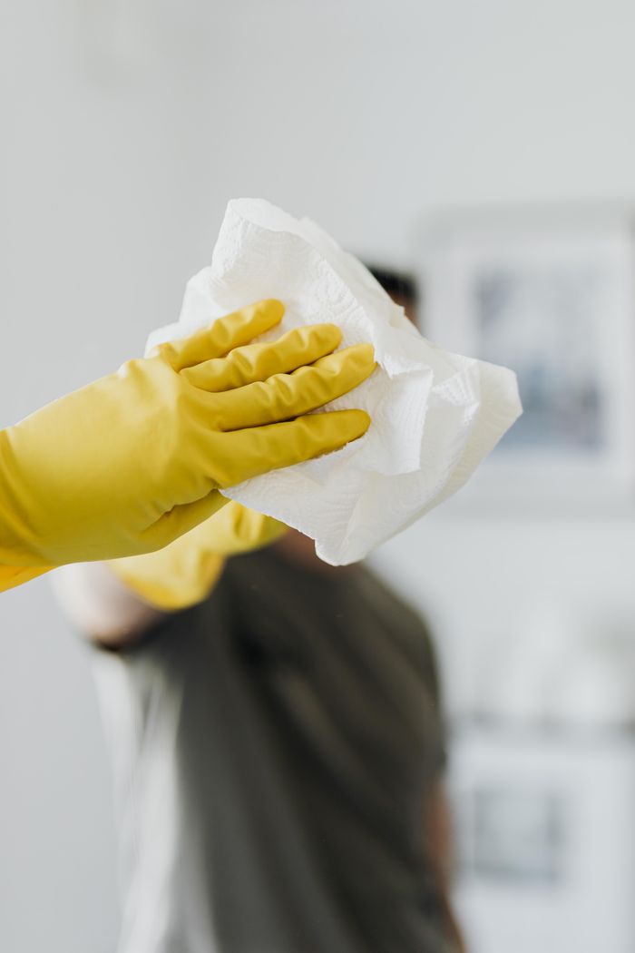 services-01 Anonymous male wearing yellow latex gloves and dark t shirt wiping mirror in bathroom with paper napkin