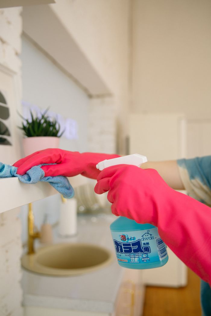 services-03 Person using spray bottle and cloth for cleaning a kitchen shelf, ensuring hygiene and cleanliness.