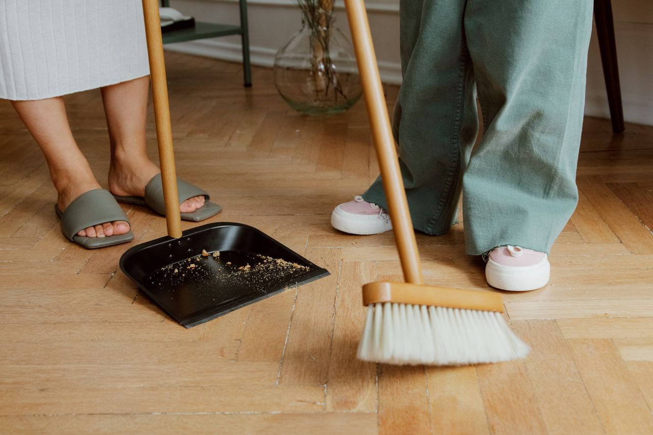 gallery-1 Close-up of people cleaning wooden floor with broom and dustpan indoors.